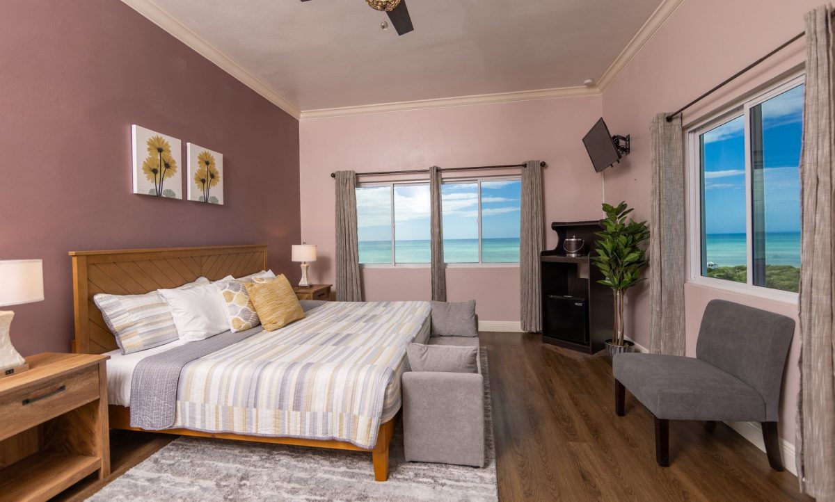 Bedroom with a bed, two chairs, and a window with a view of the ocean.