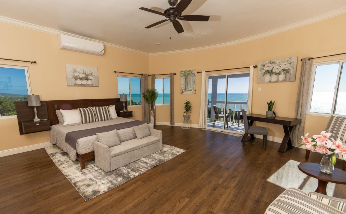 Spacious bedroom with ocean view; dark wood bed frame, rug, and furniture. Sliding door to balcony.